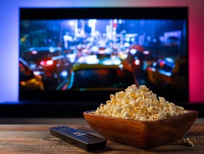 Popcorn in a wooden bowl with a tv remote beside it