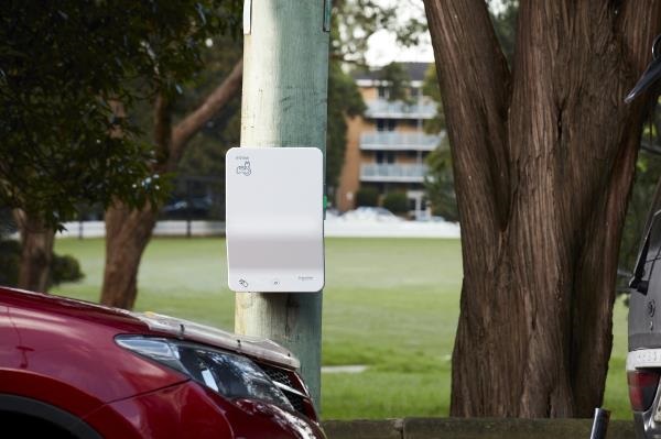 A maroon car parked on the street next to a power pole with an EV charger attached to it. A park is in the background.