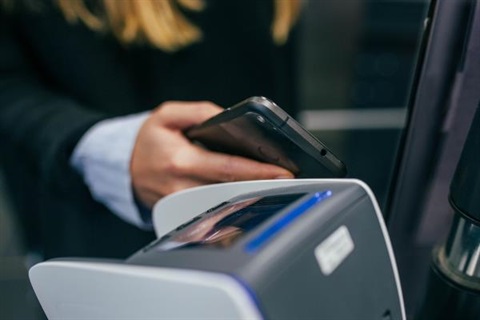 A woman taps her phone to a card reader to pay with her card