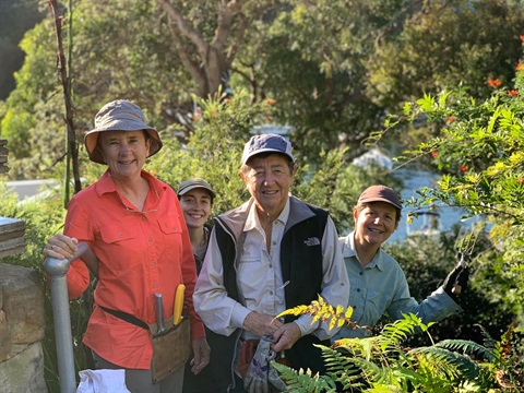 Four people are standing in local bushland, smiling at the camera. 