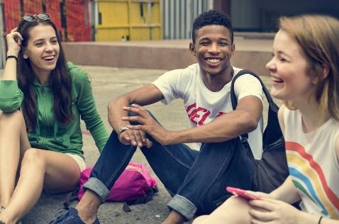 Three young people sitting on the ground smiling 